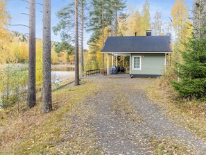A cabin with a porch, a gravel path leading to it, and a forested area in the background.