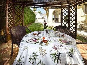 A covered outdoor dining area with a table set for a meal, surrounded by wicker chairs. - Villa Buena Vida by Interhome (Dénia)