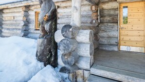 Eine Blockhütte mit einer Holz-Bärenskulptur, einer Holztür und einem Schild mit der Aufschrift 'ISO-KARHU'.
