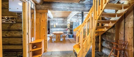 A log cabin interior with a stone floor, wooden staircase, and a dining area.