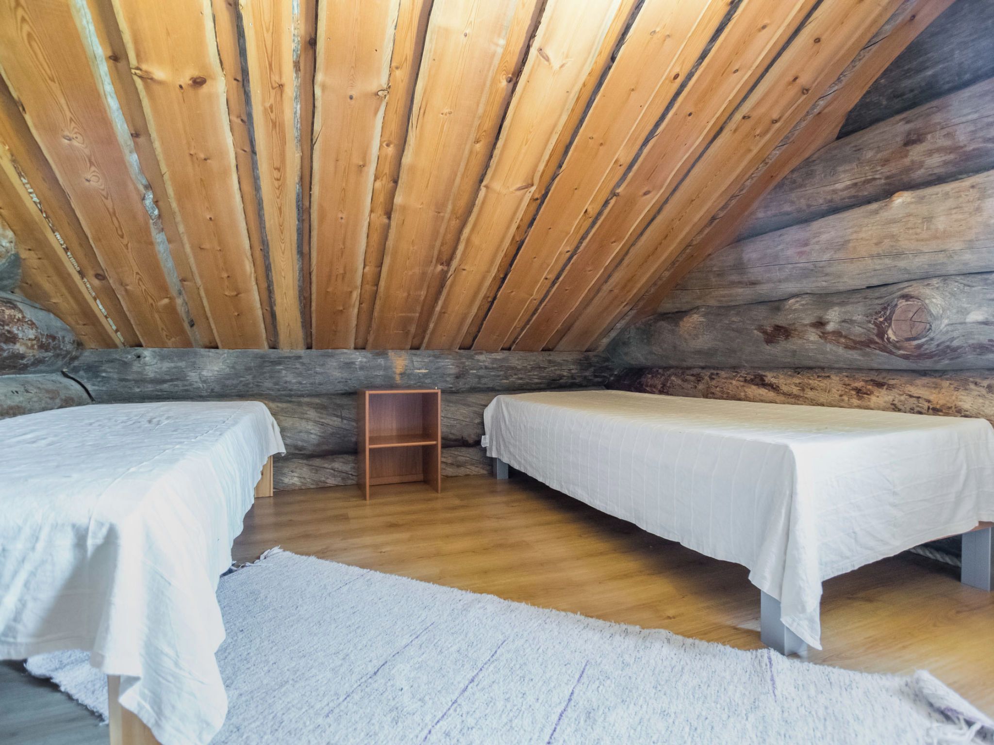 Une cabane avec deux lits, des murs en bois et un plafond en pente.