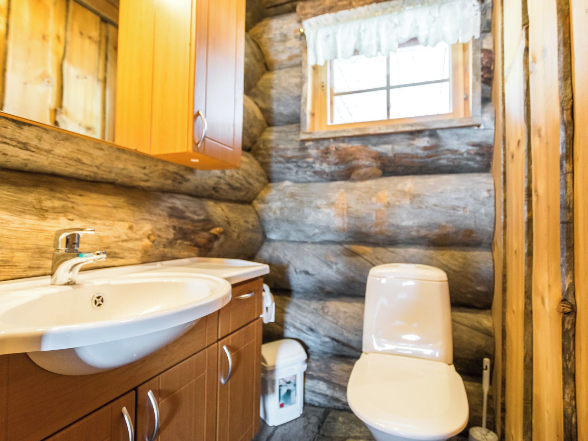 Une salle de bain au design inspiré des cabanes en bois, comprenant un lavabo, des toilettes et une fenêtre avec un rideau.