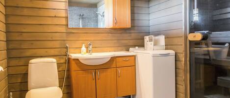 A compact bathroom with a wooden wall, a white toilet, a sink with a mirror above, and a small white washing machine.