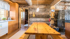 Ein rustikaler Holzraum mit einem großen Holztisch und Bänken, Holzkästen und einem Steinkamin.