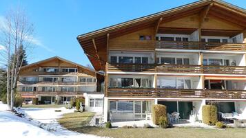 Eine mehrstöckige Holz-Chalet mit Balkonen, einer überdachten Sitzgelegenheit im Freien und einer verschneiten Landschaft.
