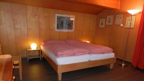 Ein Zimmer mit Holzwänden, einem Einzelbett, zwei Nachttischen mit Lampen und gerahmten Bildern an der Wand.