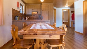 Un tavolo da pranzo in legno con sedie, un angolo cottura con mobili impiallacciati, e un corridoio che porta a un'altra stanza.