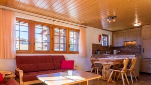 Una stanza accogliente con soffitto in legno, un divano, un tavolo da pranzo con sedie e un angolo cottura con pensili e un piano di lavoro.