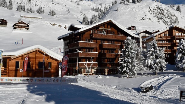 Una stazione sciistica con chalet in legno, alberi innevati e un cielo azzurro limpido.