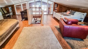 A spacious loft bedroom with a large bed, a red leather sofa, and a view of the outside through a glass door. - Arctic chalet by Interhome (Ylläsjärvi)