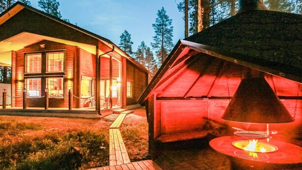 A cabin with a large windowed front and a chimney emitting smoke, surrounded by a forest. - Arctic chalet by Interhome (Ylläsjärvi)