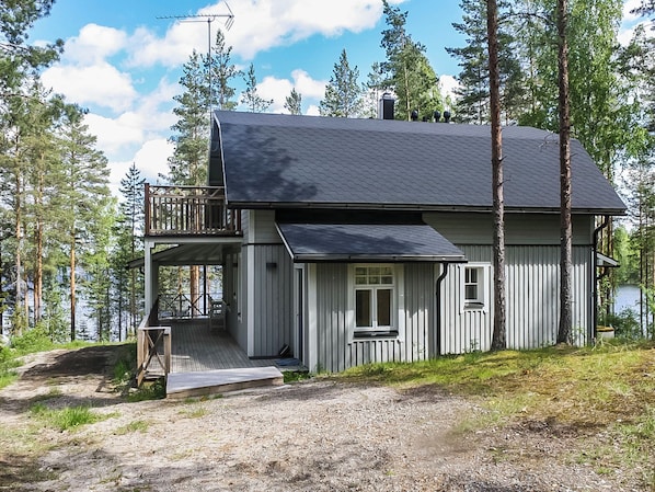 A two-story cabin with a balcony, a deck, and a small porch.