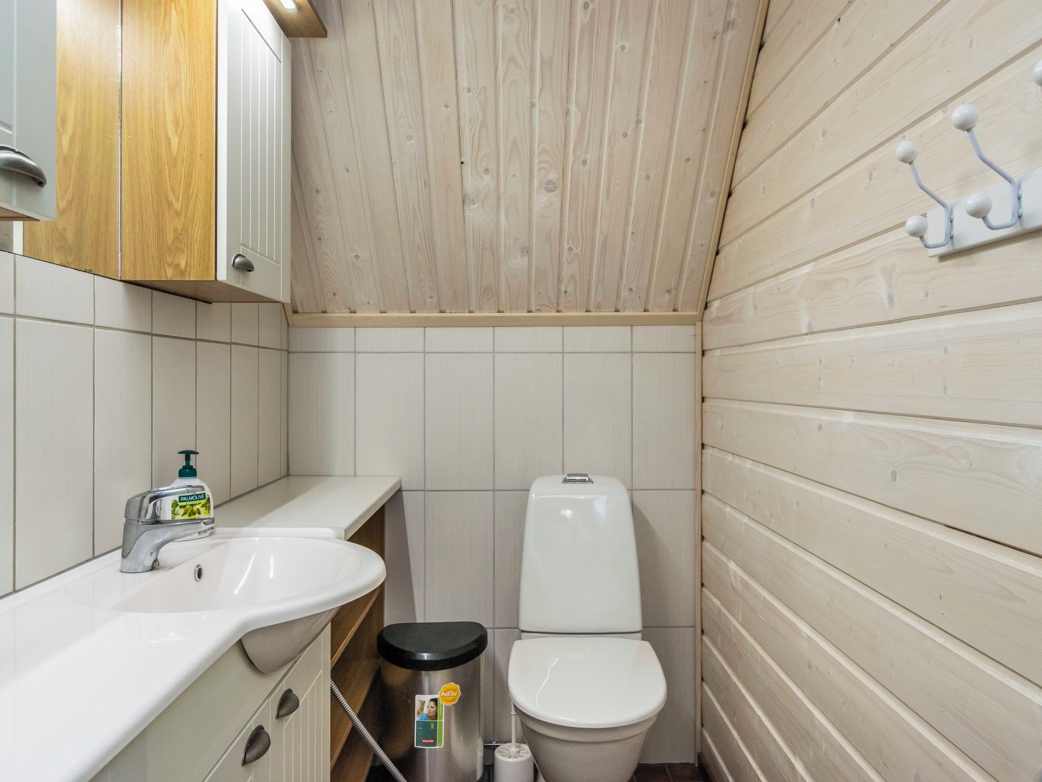Ein kleines Badezimmer mit einer Holzwand, einem weißen Waschbecken und einer Toilette.