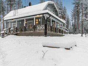 A snow-covered lodge with a wooden deck and a large windowed porch.