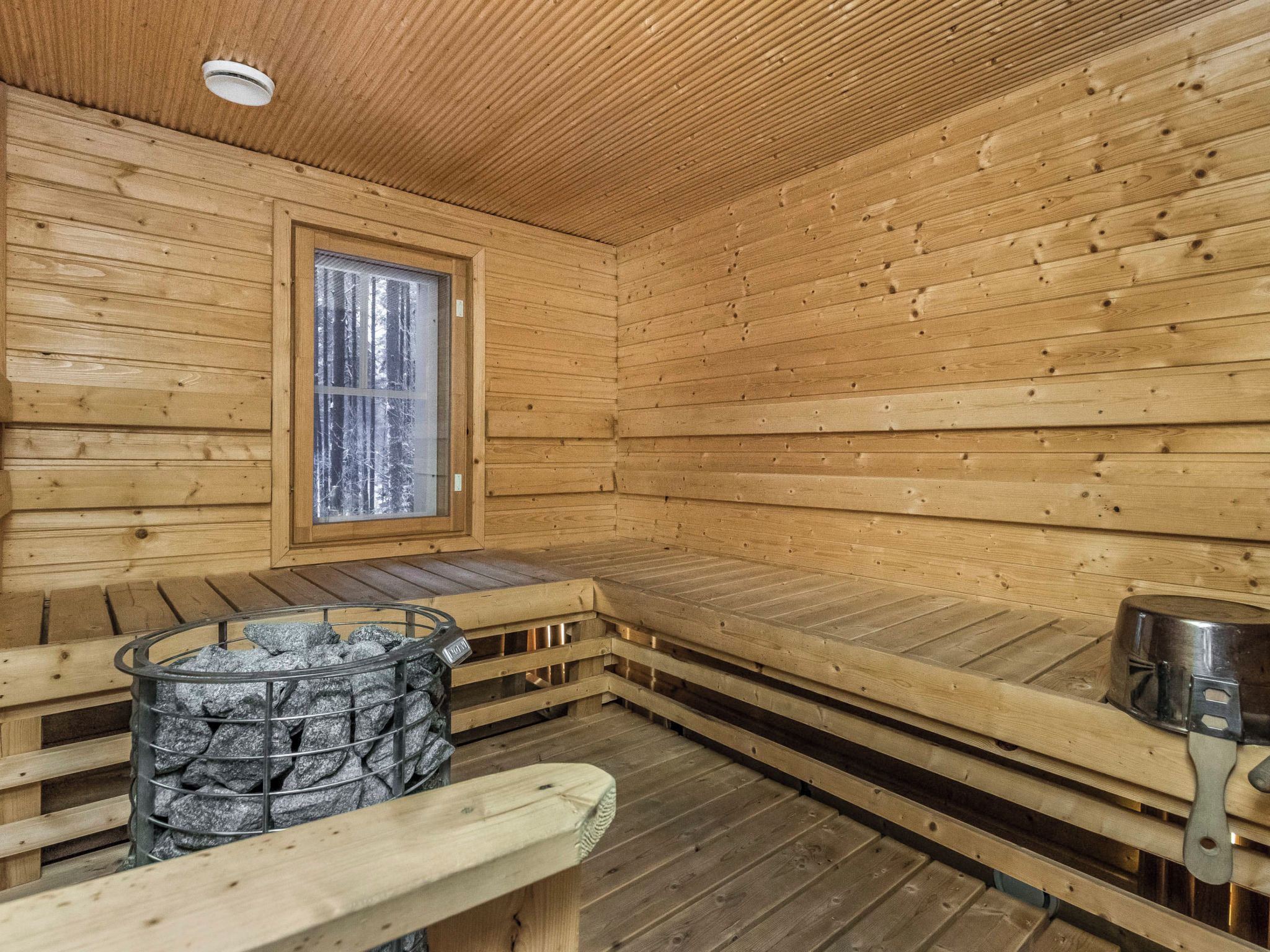 Un sauna en bois, doté de bancs, d’une fenêtre et d’un récipient rempli de pierres.