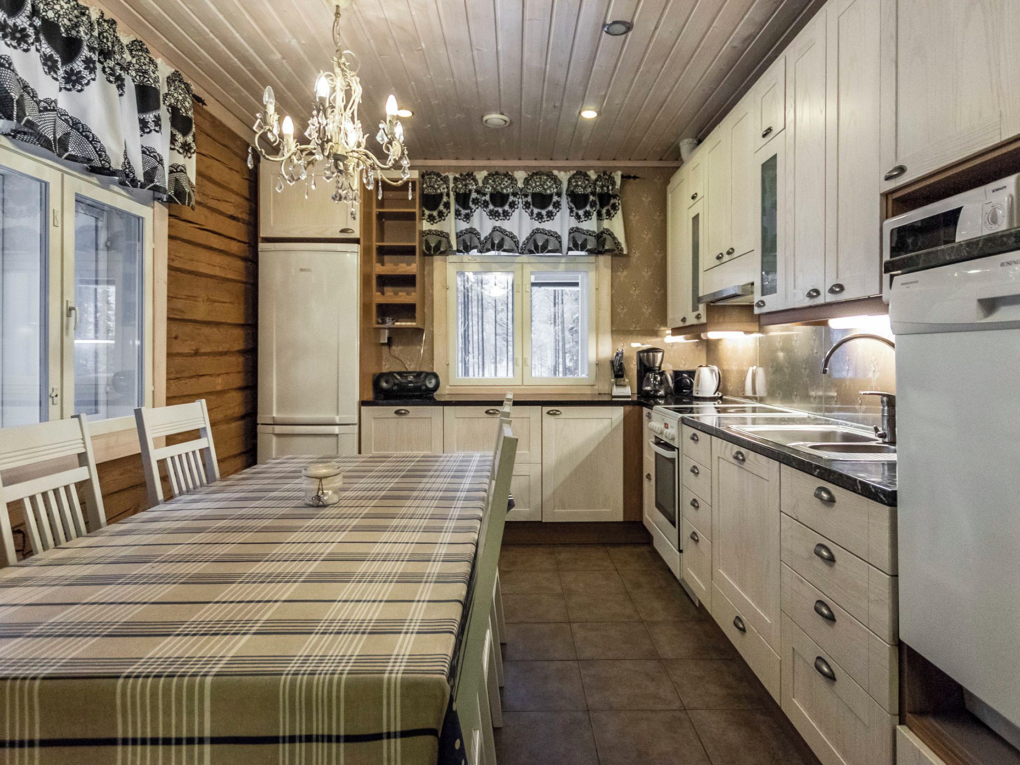 Una cocina con armarios de madera, una mesa de comedor con mantel a cuadros y una araña.