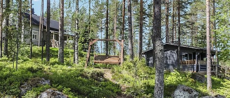 A cabin surrounded by a forest with a wooden swing bridge.