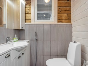 A bathroom with a wooden interior, a white sink, a toilet, and a shower.