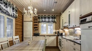 Cocina compacta con armarios de madera, una mesa de comedor con mantel a cuadros, una araña y una ventana con cortinas decorativas.