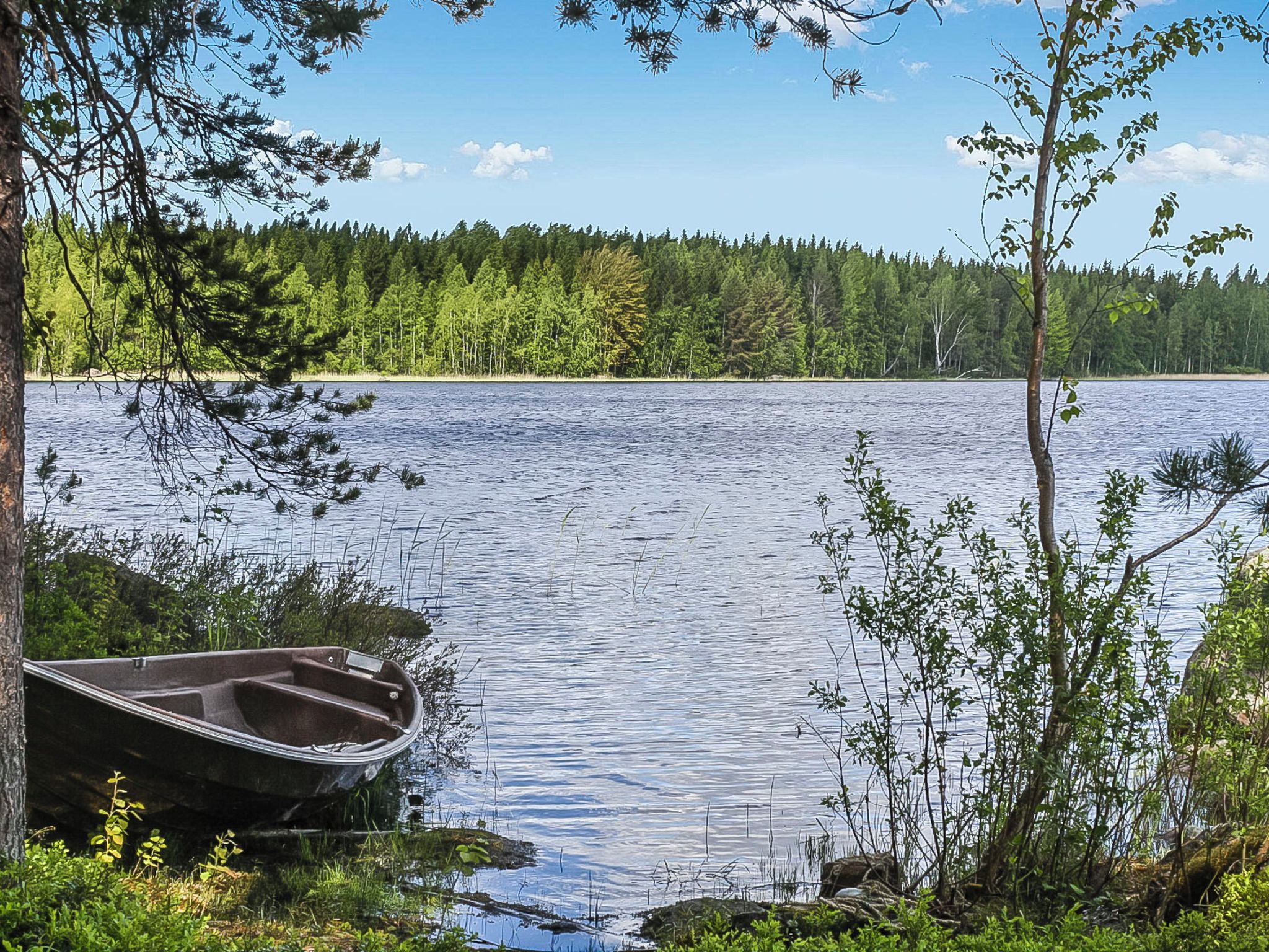 A calm lake with a small boat docked on the shore, surrounded by dense forest.