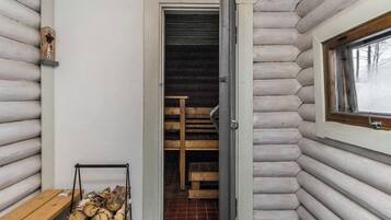 L’intérieur d’une cabane en rondins, avec un banc en bois, une porte donnant sur un espace de rangement et une fenêtre.