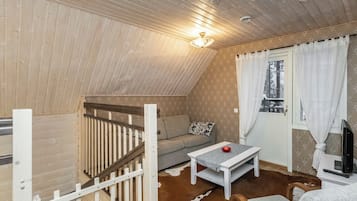 Una habitación acogedora con techo inclinado, un sofá, una mesita, un televisor y una ventana con cortinas.