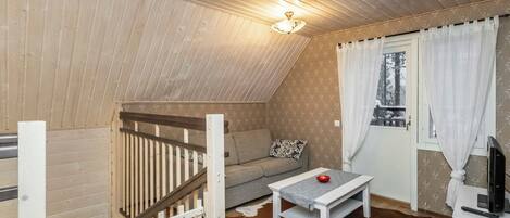 A cozy room with a sloped ceiling, a sofa, a small table, a TV, and a window with curtains.