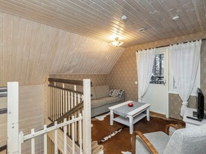 Una habitación acogedora con techo inclinado, un sofá, una mesita, un televisor y una ventana con cortinas.