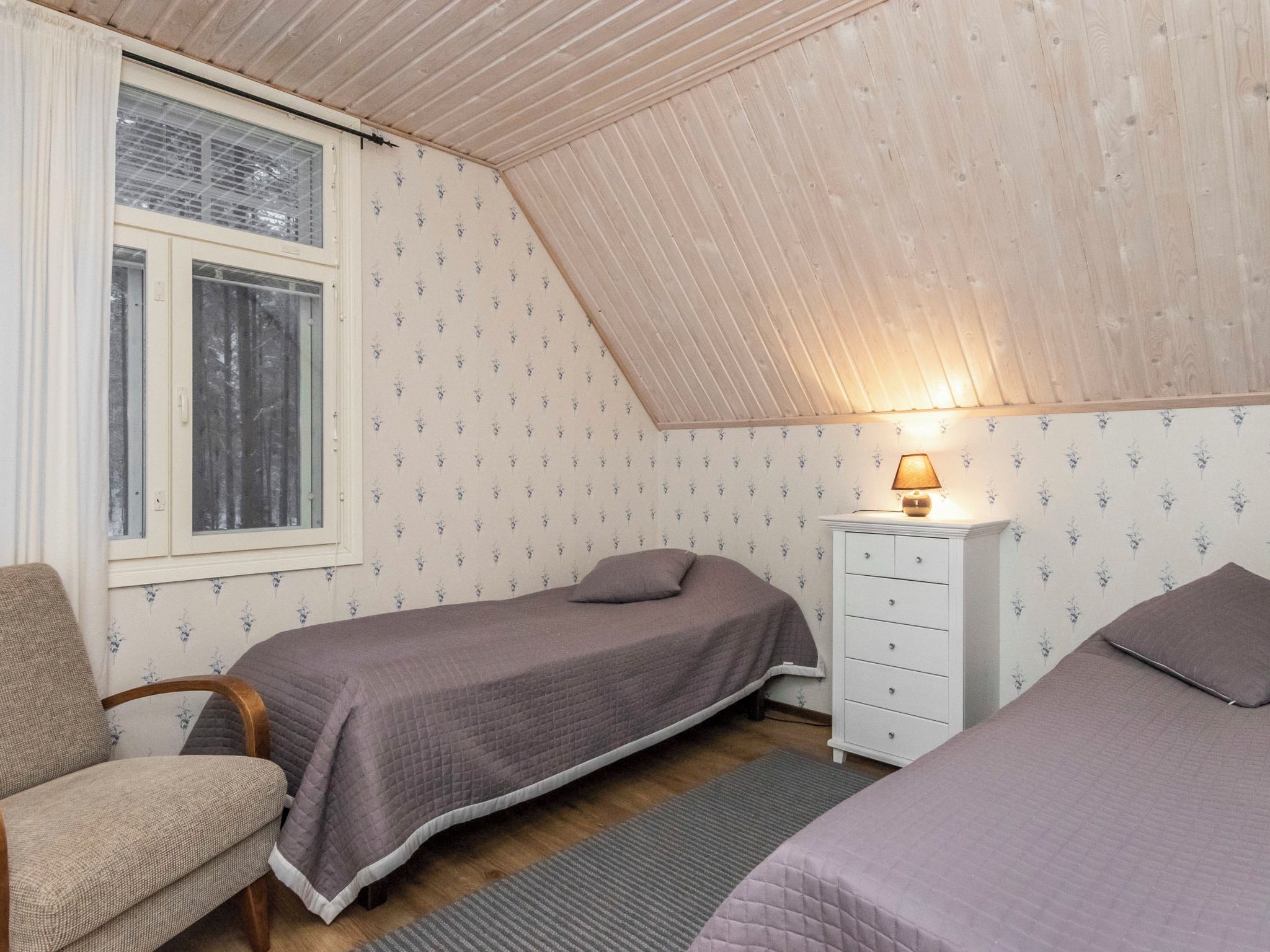 Un dormitorio pequeño y acogedor con dos camas, una mesita de noche, una silla y una ventana con persianas.