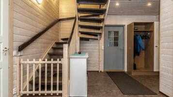 Una escalera de madera que lleva al segundo piso, una puerta con un ventanal y un perchero con ropa colgada.