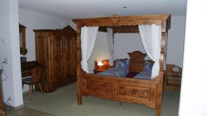 Ein Zimmer mit Himmelsbett, einem Holztisch und einem Kleiderschrank, sowie einem gefliesten Boden.