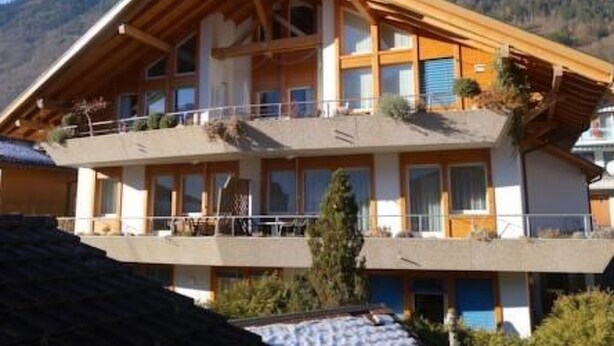 Eine zweistöckige Chalet mit Holzfassade, Balkonen und einer Bergkulisse.