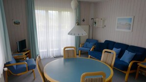 Ein Zimmer mit einem runden Tisch, blauen Sofas und Holzsesseln.