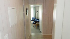 Ein schmaler Korridor mit Holzvertäfelung und Fliesenboden führt zu einem Raum mit einem blauen Sofa und einer Stehlampe.