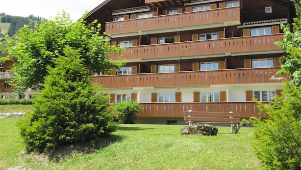 Ein mehrstöckiges Holzgebäude mit Balkonen, umgeben von Grünpflanzen.