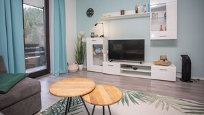 Un salon comprenant un canapé, deux tables en bois, un téléviseur et une bibliothèque.