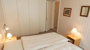 Un dormitorio con una cama, dos mesitas de noche, un armario y una puerta que da a otra habitación.