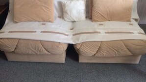 Una cama doble con ropa de cama y almohadas color beige, un cabecero con compartimentos de almacenamiento y un suelo alfombrado en color gris.