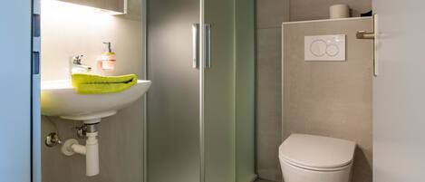 A modern bathroom with a glass shower enclosure, a white sink with a green towel, and a toilet.