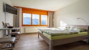 Una habitación de hotel moderna con cama, escritorio, silla, televisor y ventana con vistas a la montaña.