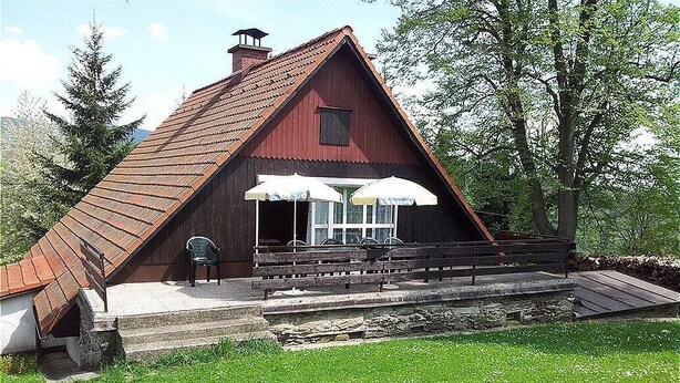 Ein rustikales Holzgebäude mit einem geneigten Dach, einer kleinen Veranda mit zwei weißen Sonnenschirmen und einer Bank.
