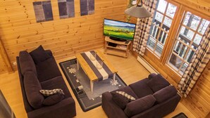 A cozy log cabin interior with two dark sofas, a wooden coffee table, a TV on a stand, and large windows with curtains. - Rukan vaarala 2 c 3 by Interhome (Kuusamo)