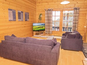 A cozy cabin interior with a large wooden wall, a television, two sofas, and a window with curtains.