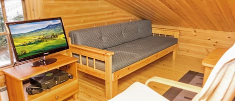 Uma cabana de madeira acolhedora com um sofá, uma televisão e uma poltrona.