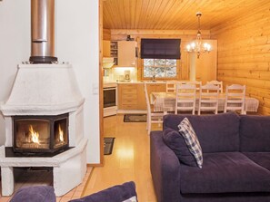A cozy cabin interior with a wood-burning stove, a dining area with chairs and a table, and a living room with a sofa.