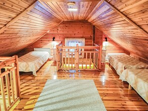 Une chambre confortable située sous les toits, avec des murs en bois et un plafond en pente, comprenant deux lits, une petite table et une fenêtre.