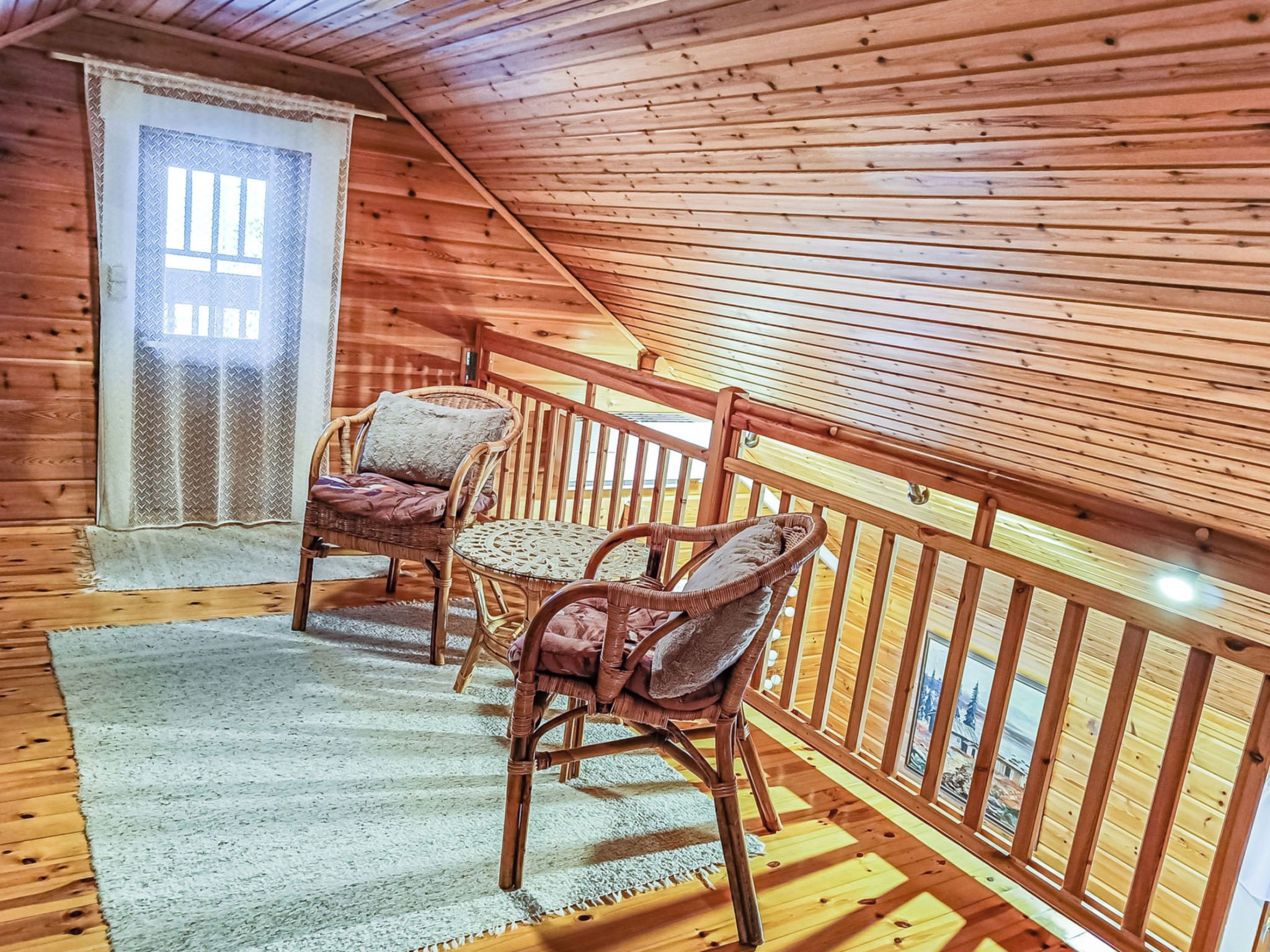 Eine Holzhütte mit geneigtem Dach, zwei Korbstühle, ein kleiner Tisch und ein Fenster mit einem Metallgitter.