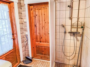 A bathroom with a wooden door, a shower with a handheld showerhead, and a tiled floor.