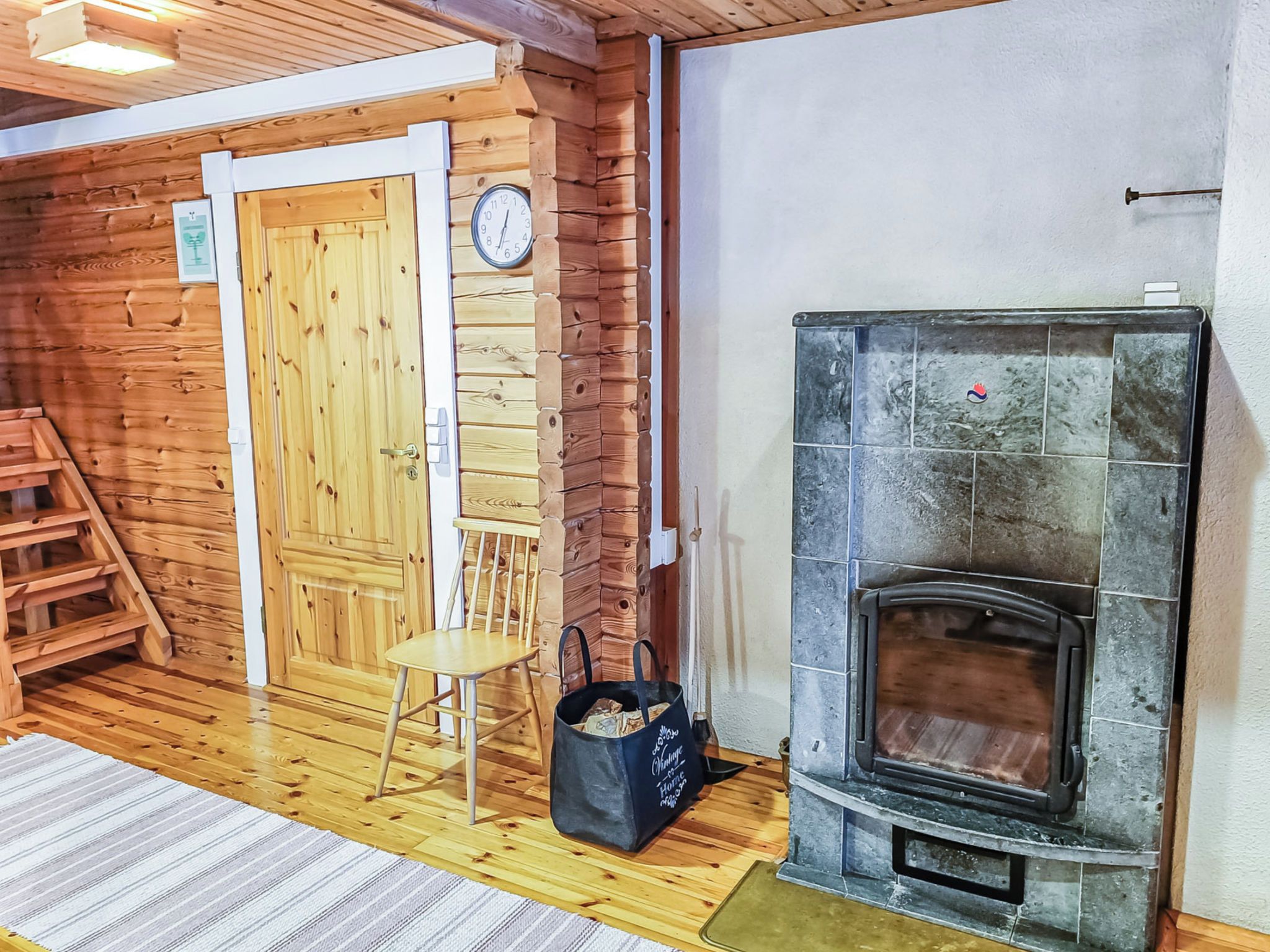 A wooden interior with a fireplace, a door, a chair, and a bag on the floor.