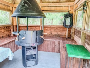 A rustic wooden cabin interior with a metal grill structure, wooden benches, and a table.